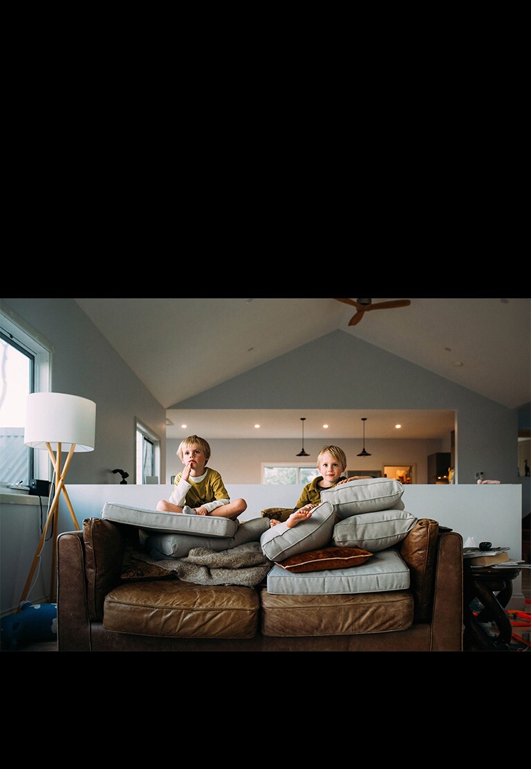 Two twin boys are watching something sitting on a sofa.