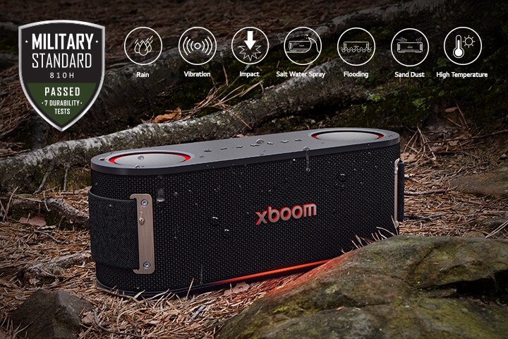 xboom Bounce is placed on soil covered with wet leaves, between a tree root and a stone. On the above left side Military standard logo is placed.	