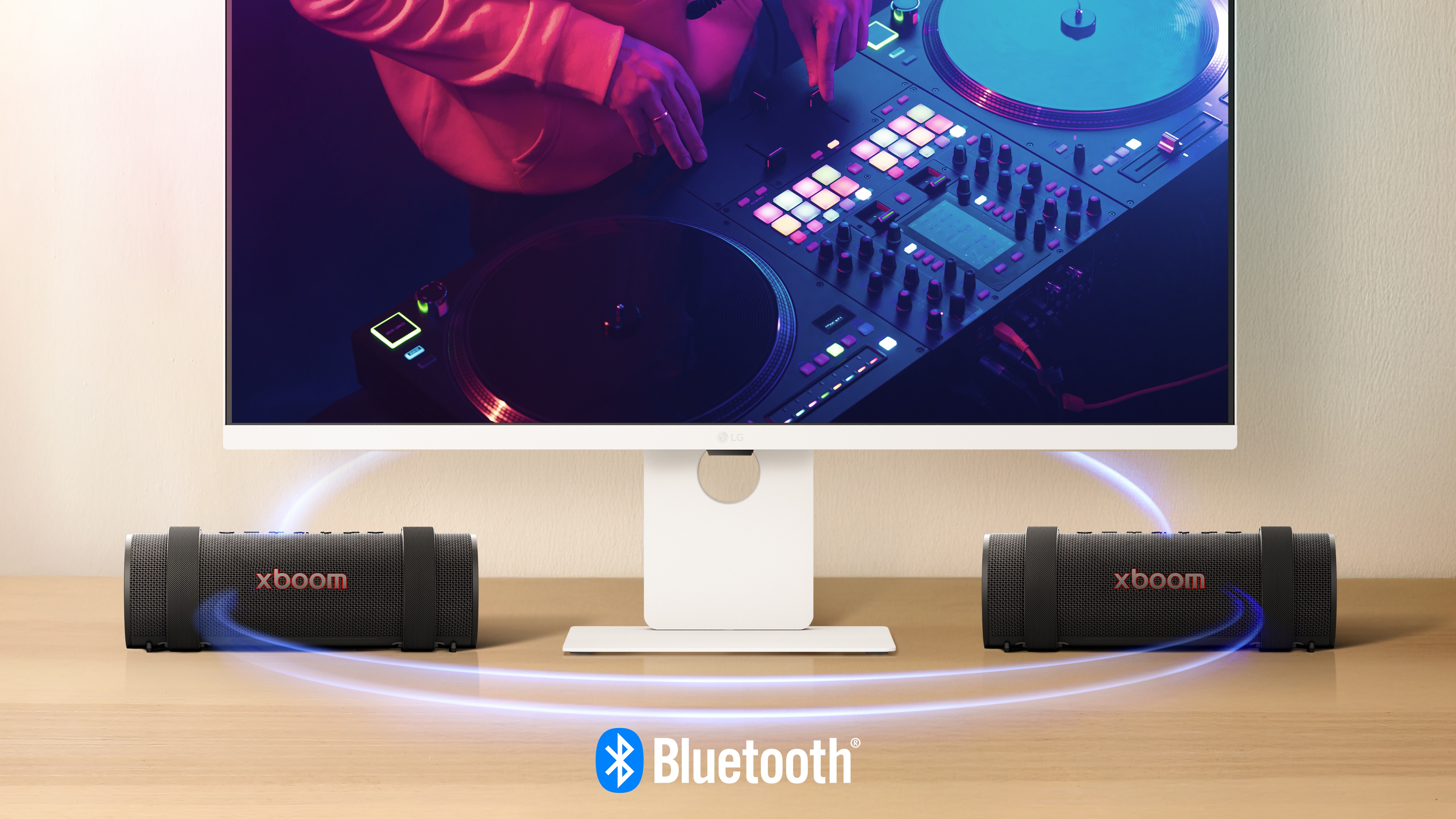 LG Smart Monitor is showing a DJing scene and two units of xboom Grab are placed on both side of the monitor. Virtual blue light streak is connecting all 3 of them to show they're connected via bluetooth. 	