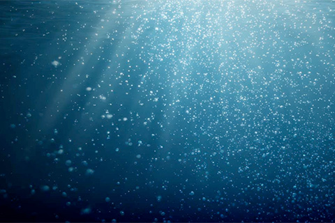 Underwater scene with light rays and fine bubbles drifting in deep blue water
