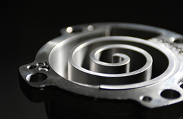 Close-up view of a metallic spiral compressor component with a sleek, polished surface against a dark background.