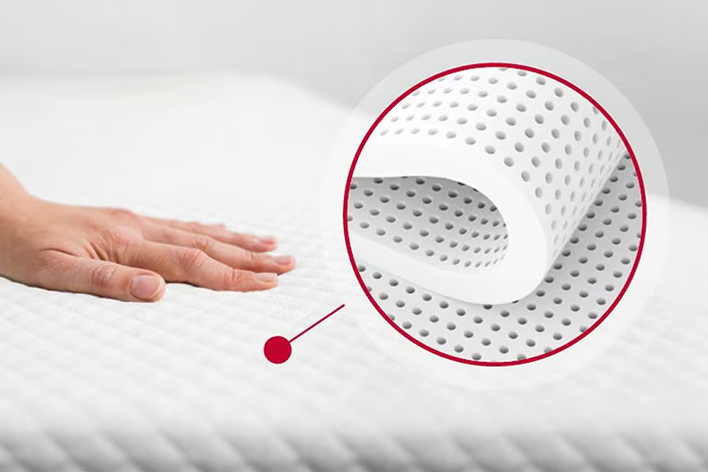 Hand pressing into a white foam mattress surface, showing its texture and softness.