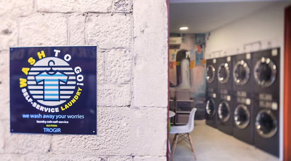 Exterior wall with Wash to Go self-service laundry sign and view into laundromat with LG washers