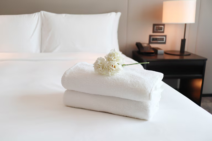 Hotel room bed with folded white towels and flower decoration
