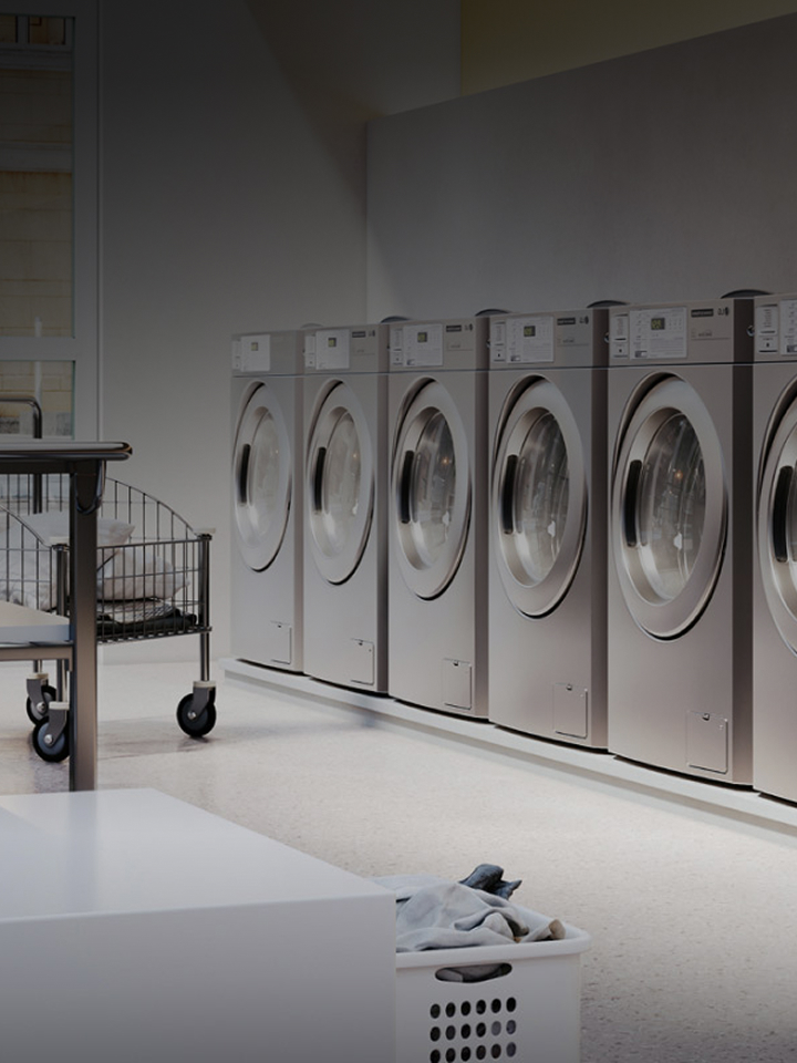 Row of LG commercial washing machines and dryers in a professional laundry facility, text overlay LG commercial laundry solutions