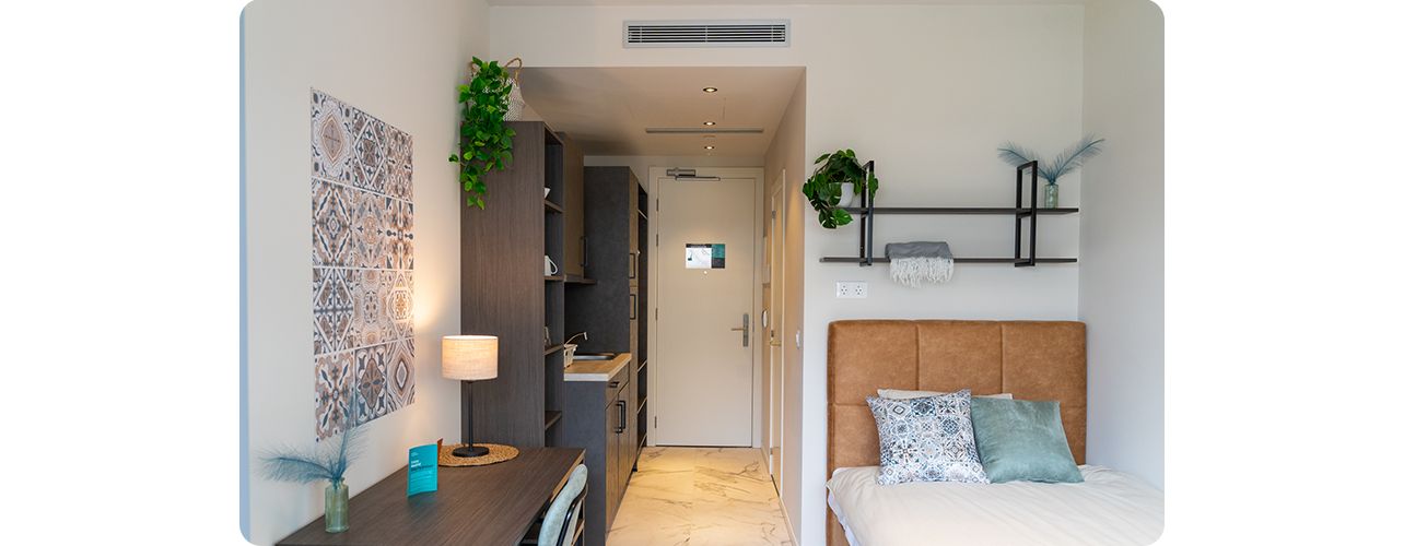 A compact room featuring a bed, a desk, and a small kitchen area, designed for efficient living and comfort.