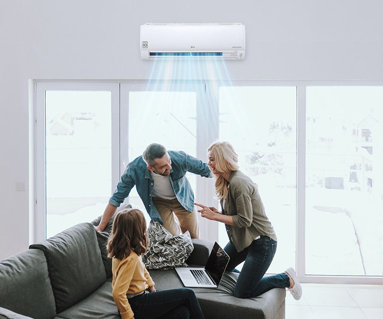 A wall-mounted air conditioner supplying blue-colored air stream in a living room while three family members smiling at each other on a sofa