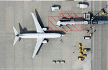Top-down view of an airplane at an airport gate with service vehicles around.