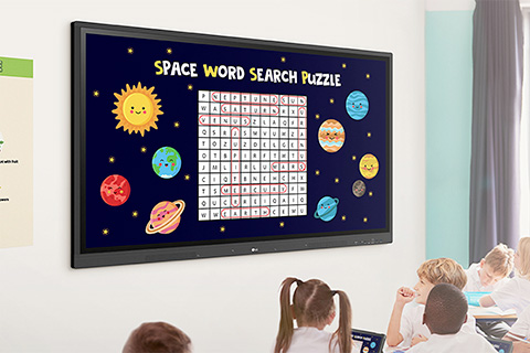 Classroom scene with children seated at desks watching a large screen displaying a 'Space Word Search Puzzle' with planets and stars around the puzzle grid.