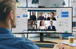 Man participating in a video conference call on an ultrawide curved monitor displaying multiple people and data charts.