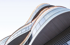 Modern glass building with curved architectural design viewed from below.