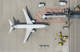 Top-down view of an airplane at an airport gate with service vehicles around.