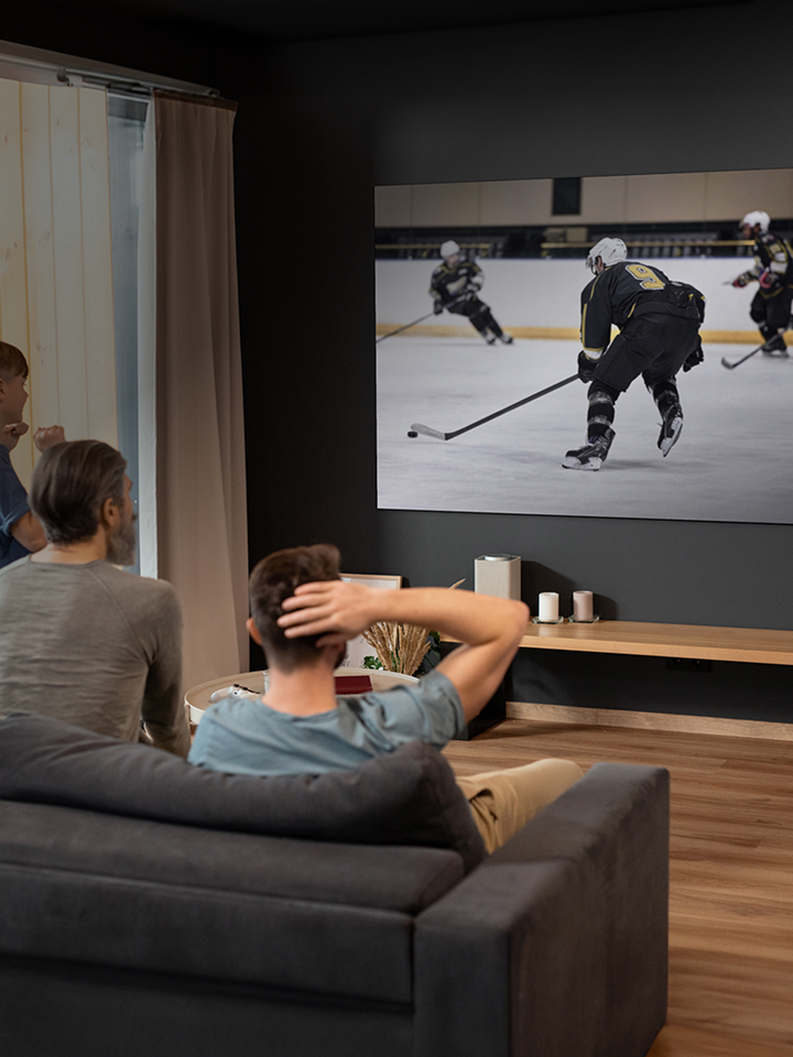People sitting in a living room watching an ice hockey game on a large wall-mounted TV screen.