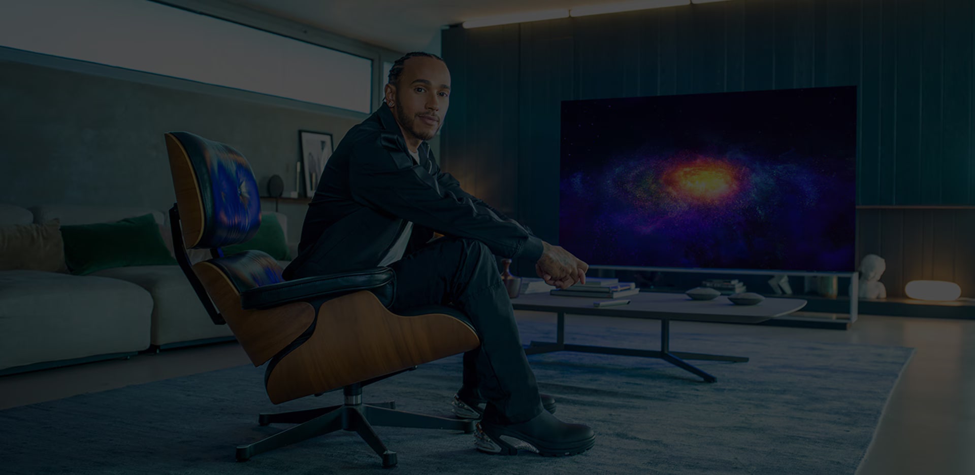 Lewis Hamilton sitting on a couch and behind him is the LG SIGNATURE OLED 8K TV.