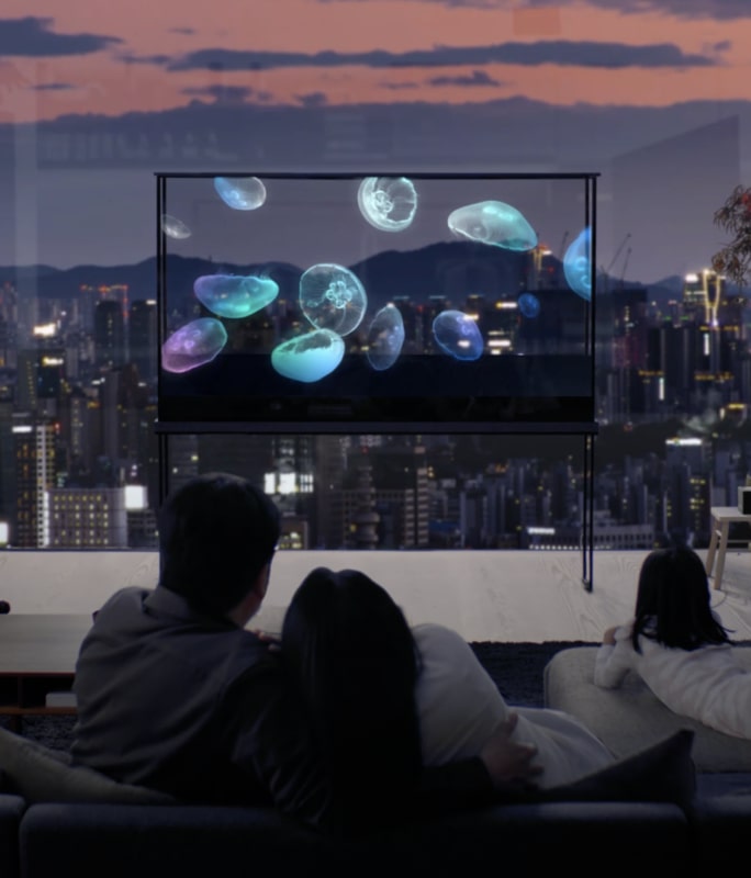 Uma família desfruta de um LG Oled T com uma água-viva flutuando, enquanto a paisagem urbana brilha através da tela transparente.