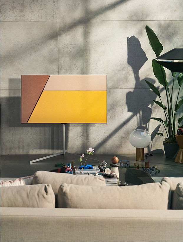 En un moderno espacio gris frente a una ventana que muestra una piscina hay un televisor LG OLED. En un espacio neutral con ladrillos a la vista, detalles de madera y vegetación hay un televisor LG OLED.	