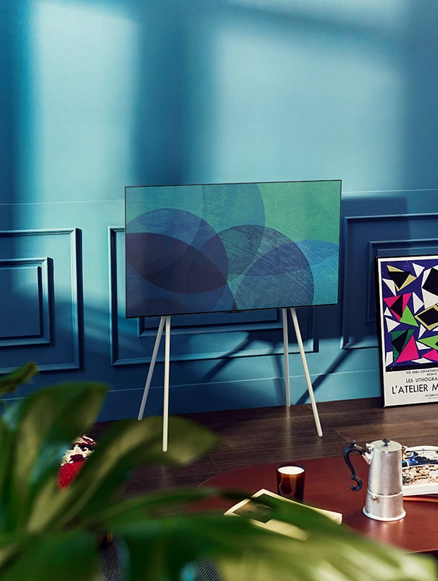 En una moderna habitación gris frente a una ventana que da a un bosque nevado hay un televisor LG OLED con soporte Gallery. En una colorida sala de estar con muebles de madera y tonos pastel hay un televisor LG OLED con soporte de suelo.