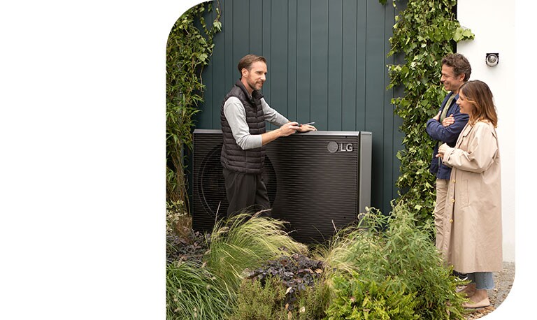 An engineer man is standing next to the new black colored THERMA V, talking to a young couple while installing LG Air to Water Heat Pump.