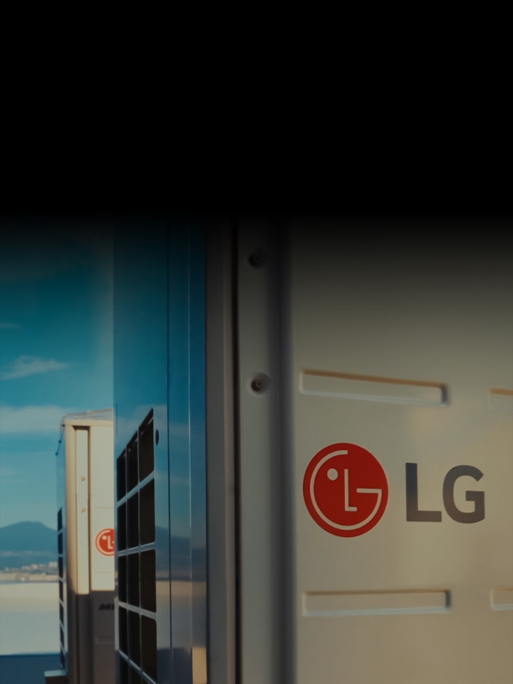 There are several LG HVAC products on the rooftop of a high-rise building. There is a mountain behind the products. 	