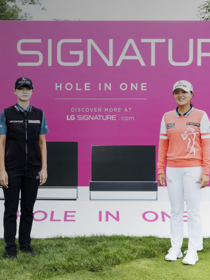 A pink LG SIGNATURE ad on a golf course, featuring product images with two people standing in the foreground against a verdant landscape.