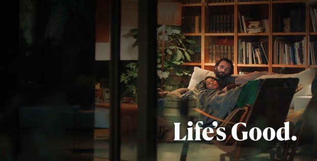 A man and a woman are lying on a sofa, looking relaxed and happy. At the bottom of the image, “Life’s Good.” is written in white.