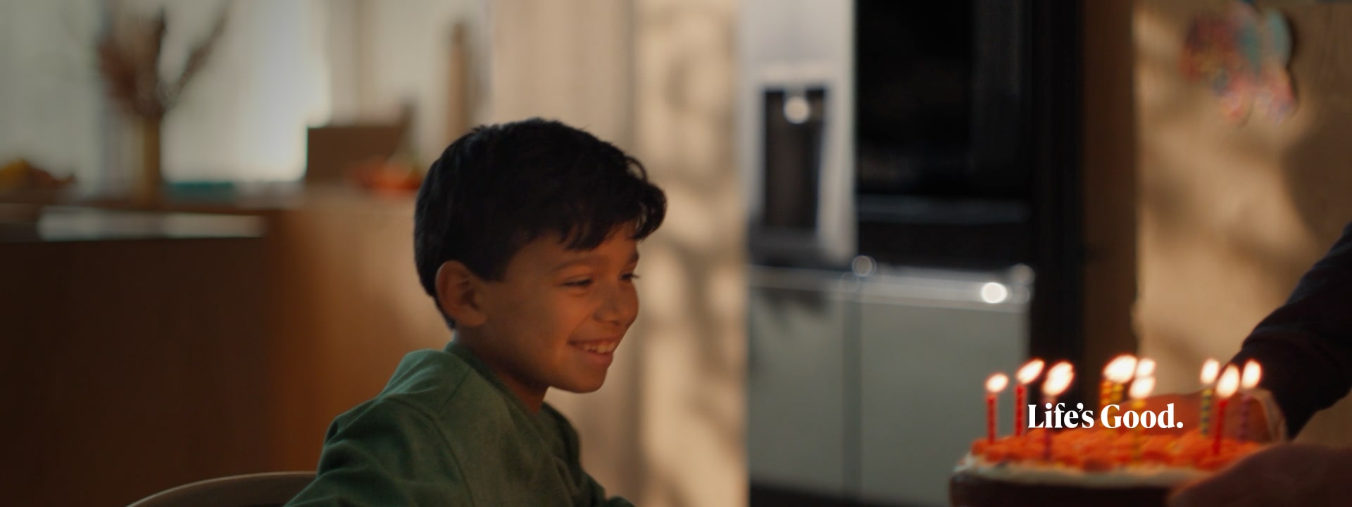 The child's face is clearly visible in front of the candlelit cake, and the LG InstaView refrigerator is faintly visible in the background.