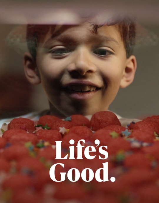 A smiling child admiring strawberries on the top of a cake, looking happy and excited.