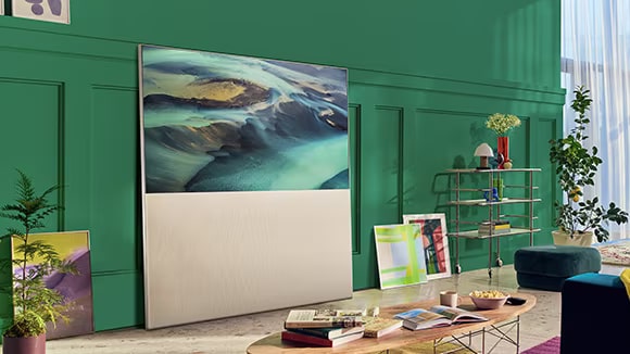 EASEL in Full View Mode leunt tegen een groene muur in de woonkamer en wordt omgeven door kunst. Er is een scène van zandduinen op het scherm.