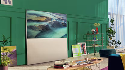 EASEL in Full View Mode leunt tegen een groene muur in de woonkamer en wordt omgeven door kunst. Er is een scène van zandduinen op het scherm.