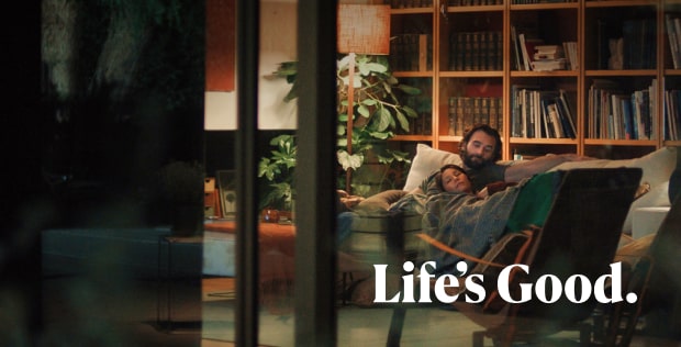 A man and a woman are lying on a sofa, looking relaxed and happy. At the bottom of the image, “Life’s Good.” is written in white.
