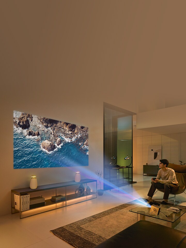 Un hombre sentado en el sillón disfrutando un video en 4K en una gran pantalla proyectada en la pared del salón con el CineBeam Q HU710PB y bocina XBOOM.