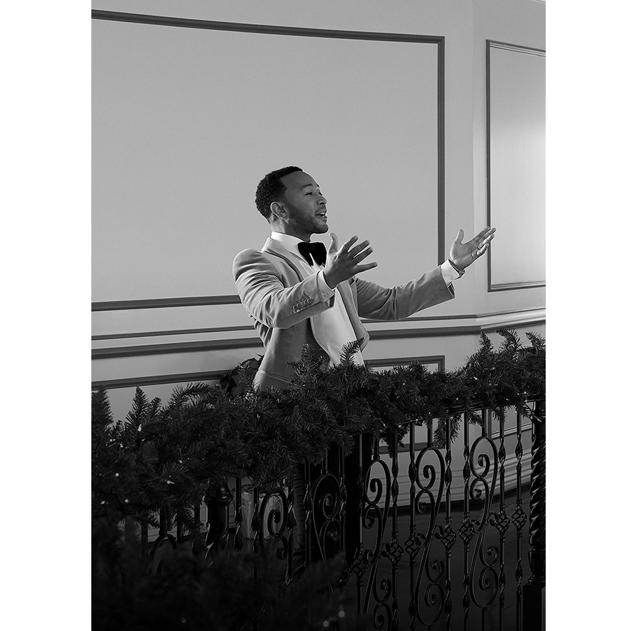 Singer John Legend walking down a staircase holding onto a handrail decorated with Christmas decoration.