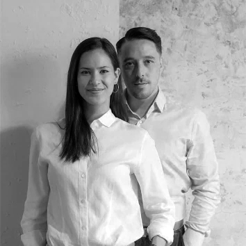 A man and woman stood in front of a grey wall.